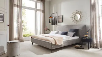 Modernes Schlafzimmer mit dem Polsterbett „Sweet Dreams“ von Bielefelder Werkstätten in grauem Stoffbezug. Das elegante Design mit hohem Kopfteil und schlanken Metallfüßen schafft eine ruhige, einladende Atmosphäre. Erhältlich bei himmlisch wohnen.